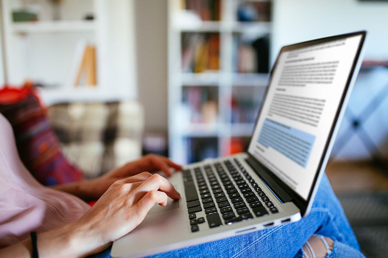 A woman engrossed in her work, sitting on a couch with a laptop, ensuring a seamless customer experience.