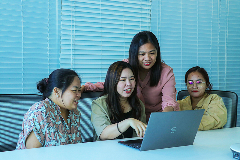 A group of women in an office, focused on a laptop, engaged in back office services.