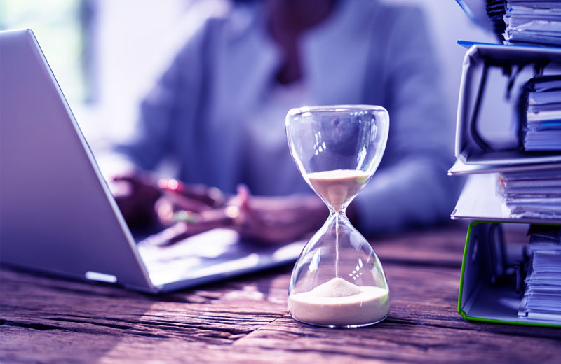 Focused professional working on web application development with a sand timer nearby.