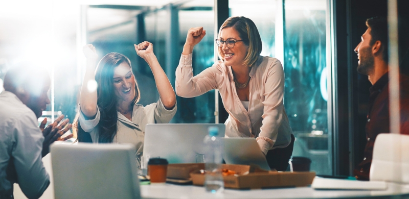 Office workers celebrating achievements, arms raised, engaged in business process outsourcing.