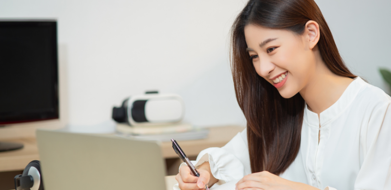 A woman happily writes on a paper, engaged in online English learning.