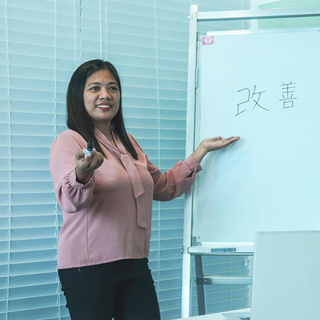 A woman stands in front of a whiteboard with Japanese characters, discussing business solutions.